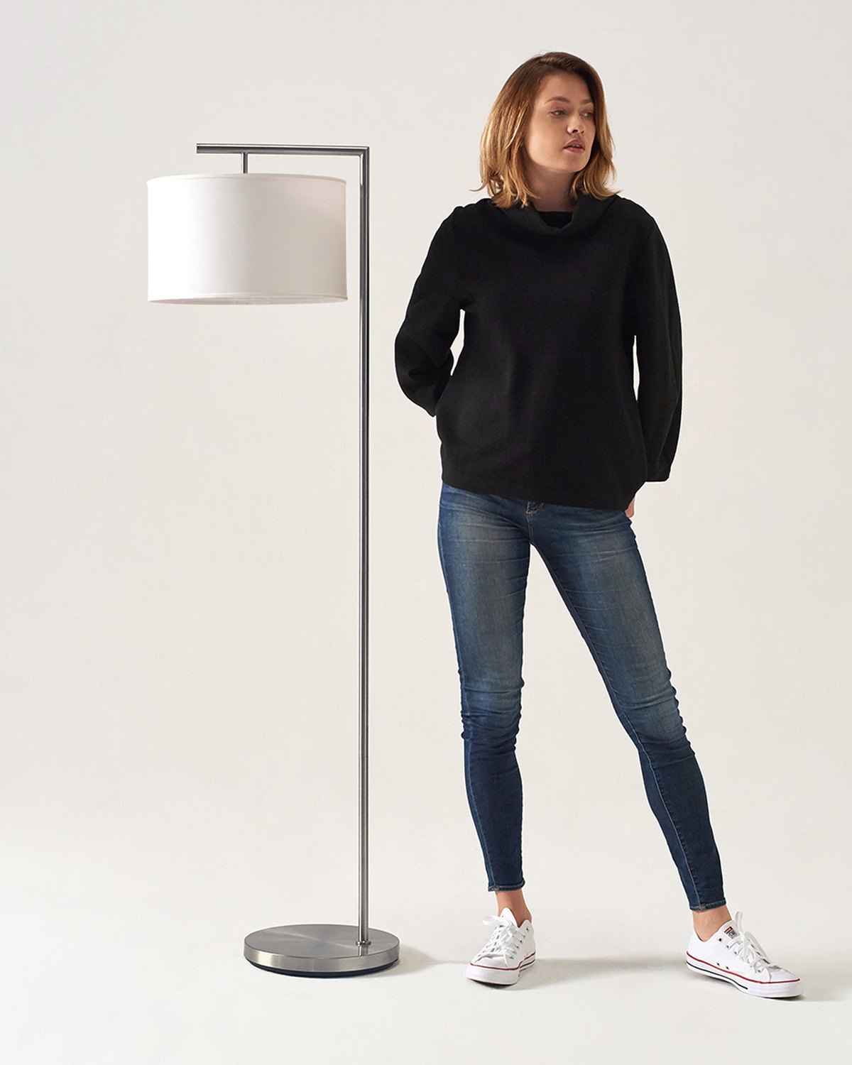 Silver Brightech Montage Modern floor lamp with a white drum shade next to a standing woman for scale