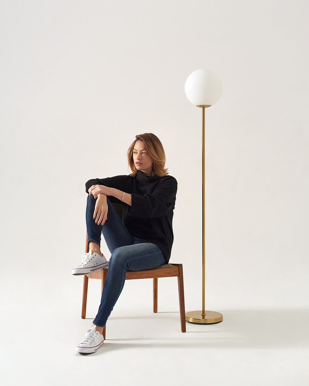 Brightech Luna floor lamp with a frosted glass globe on an antique brass stem beside a wooden chair