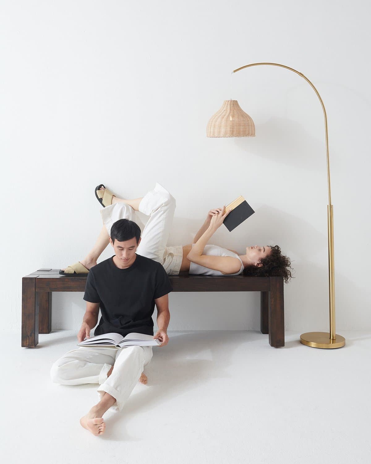 Brass Brightech Lark arc floor lamp with a rattan shade above two people relaxing on a bench