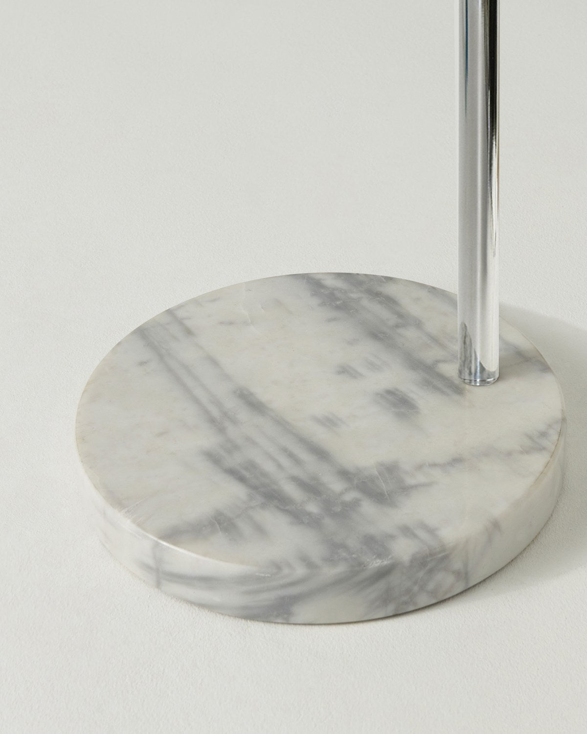Close-up of the round white marble base of the chrome Brightech Olivia arc floor lamp