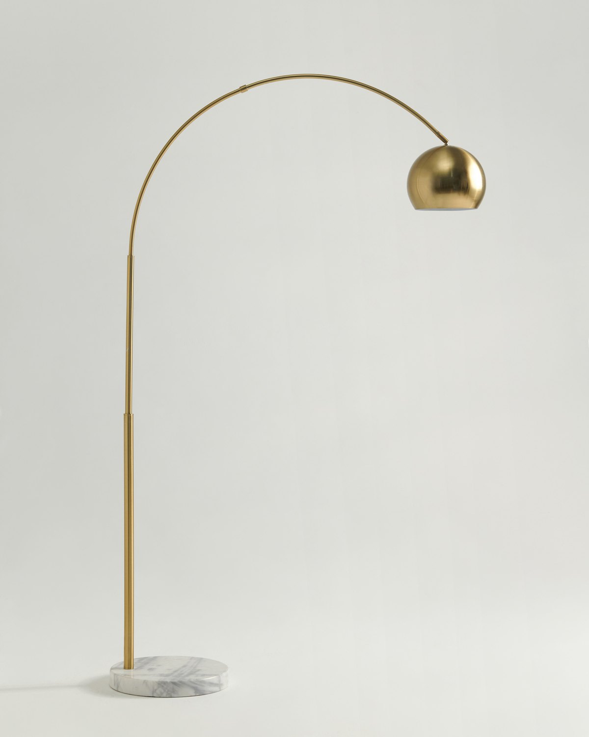 Brass Brightech Olivia arc floor lamp on a white marble base against a light grey background