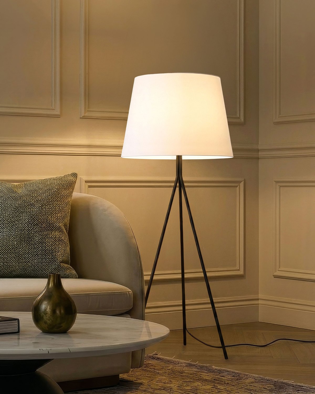 Lit Brightech Forge floor lamp with an oversized fabric empire shade on a black tripod base beside a curved sofa