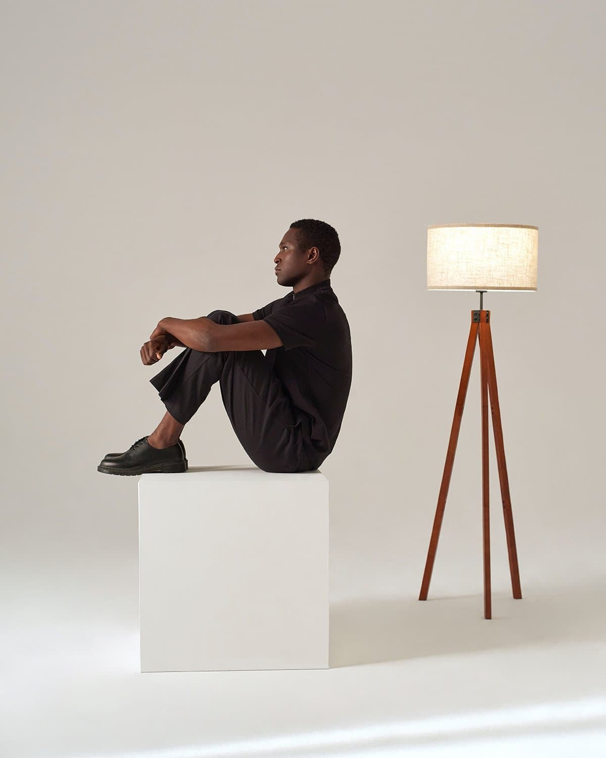 Man sitting on a block beside a lit Brightech Eden wood tripod floor lamp