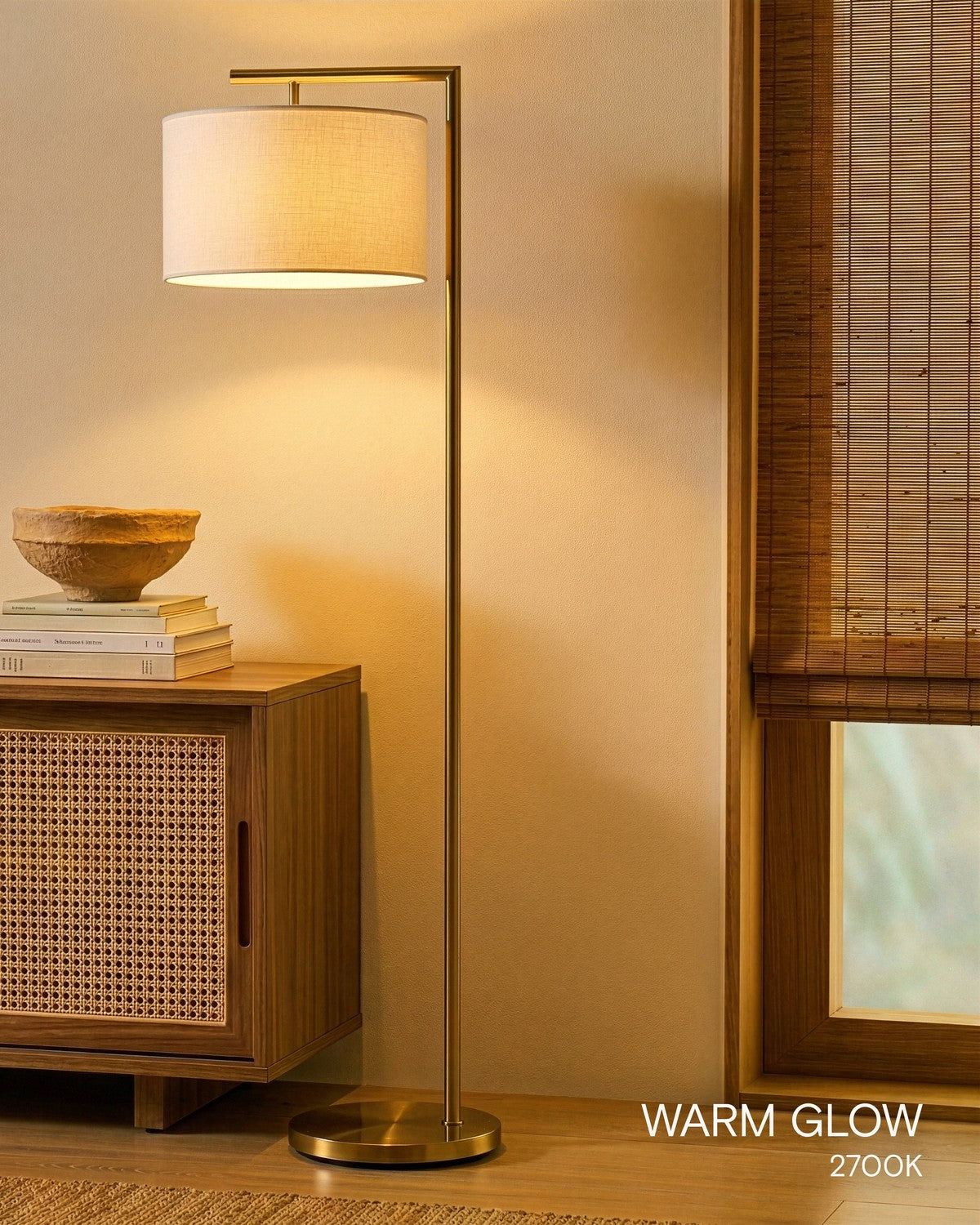 Brightech Montage Modern floor lamp with a white drum shade glowing at its warm 2700K setting beside a rattan sideboard