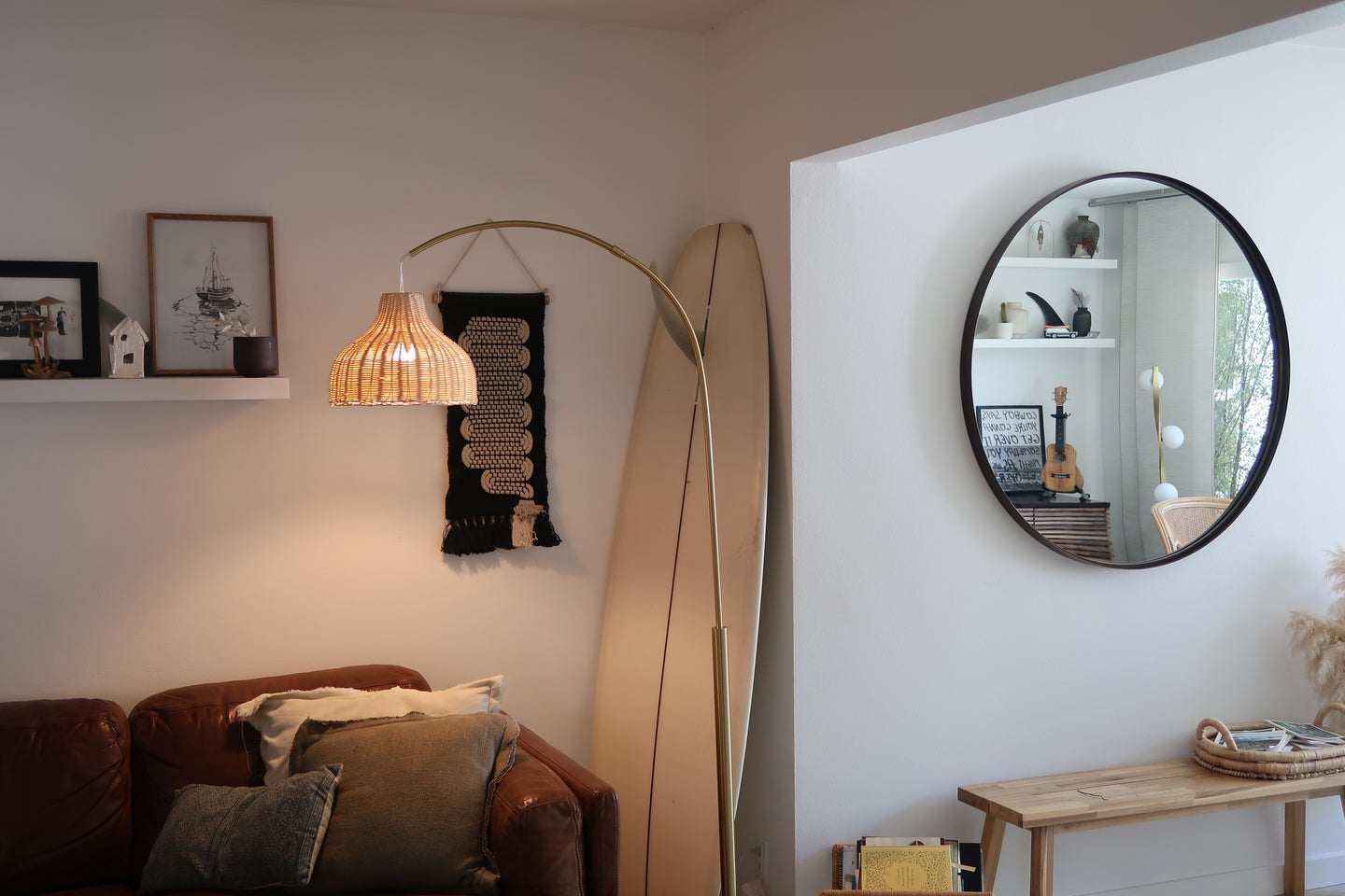 Living room with a brown sofa, floor lamp, and round mirror on a white wall.