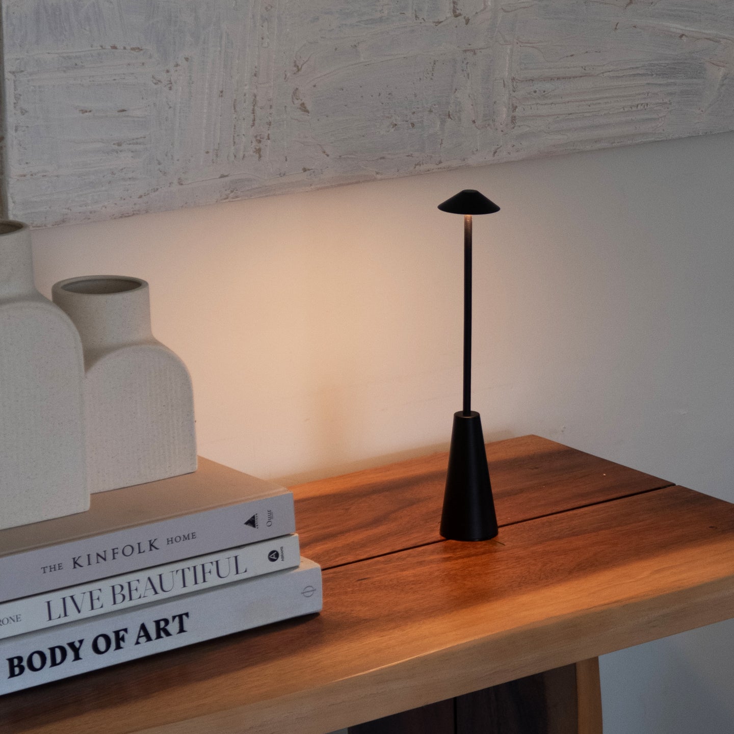 Black table lamp on a wooden surface with books and decorative items.