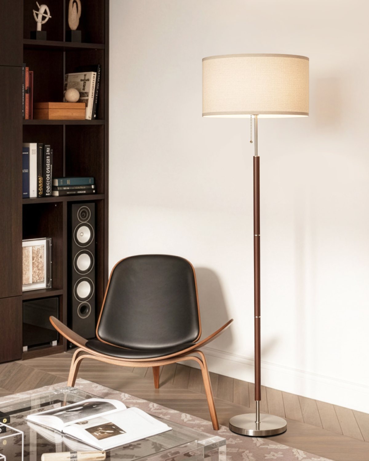 Brightech Carter floor lamp with a walnut finish stem and linen drum shade beside a black lounge chair and bookshelf