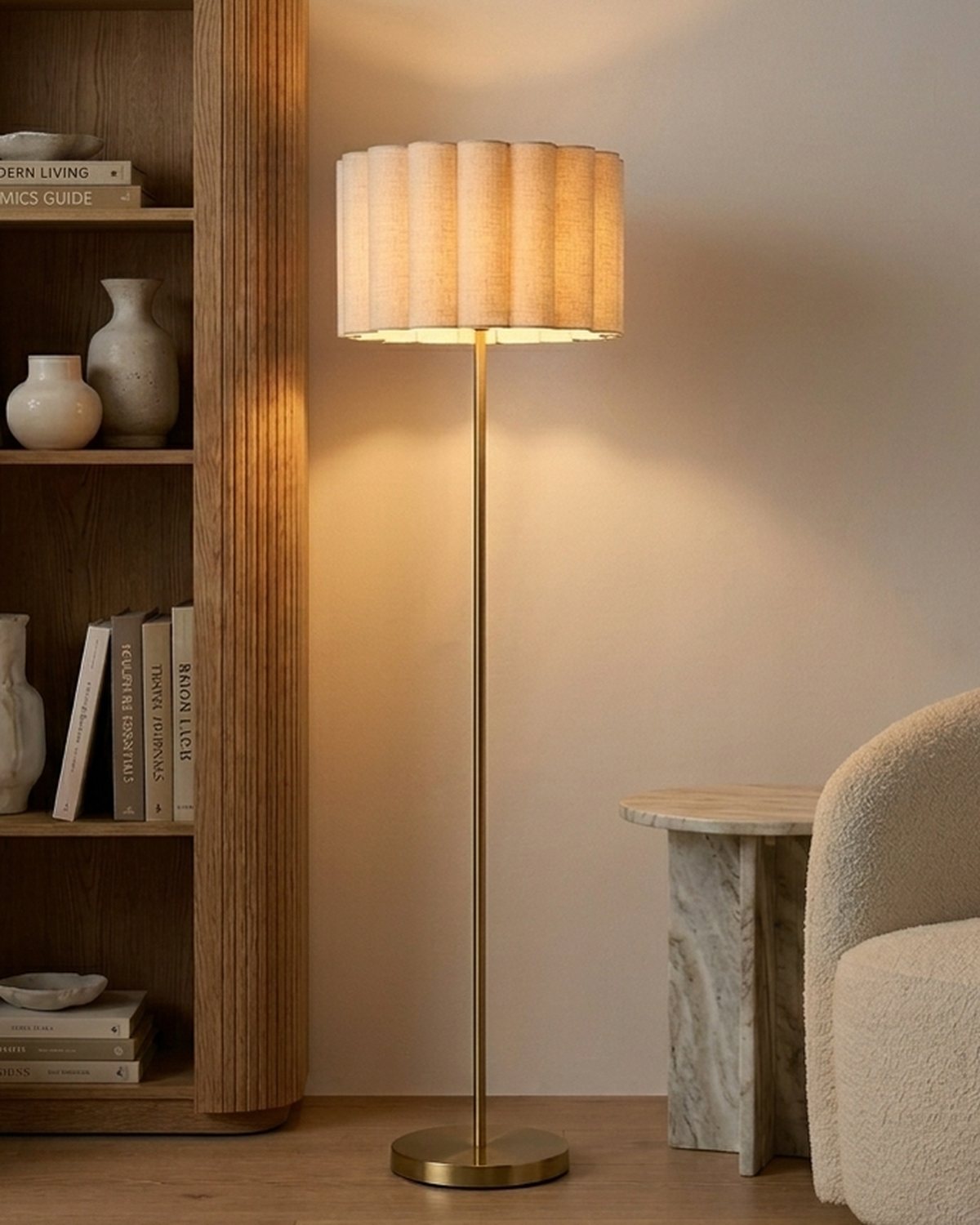 Brightech Estelle floor lamp with a scalloped ivory shade and brass stem lit beside a bookshelf and a boucle chair