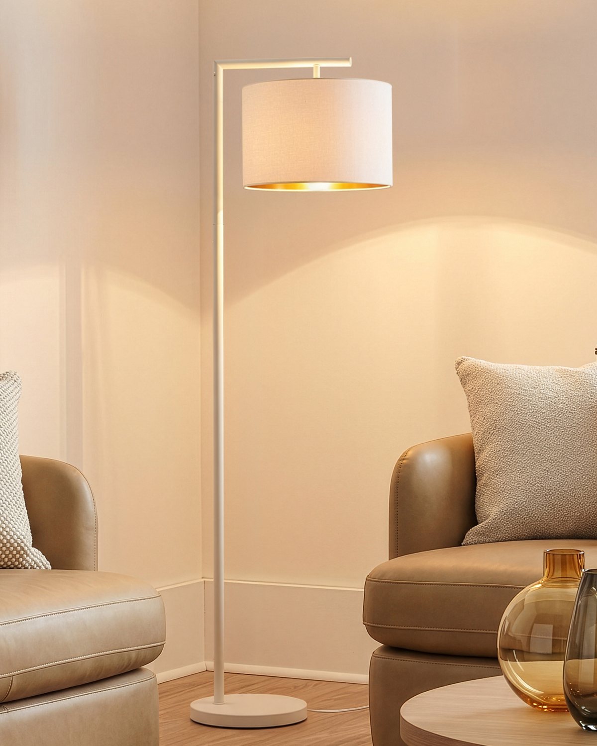 Cream Brightech Montage Modern floor lamp with a gold-lined drum shade glowing in a living room with leather sofas