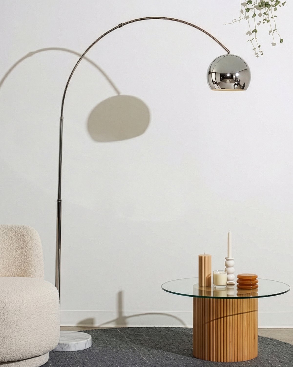 Chrome Brightech Olivia arc floor lamp curving over a boucle chair and a round glass coffee table