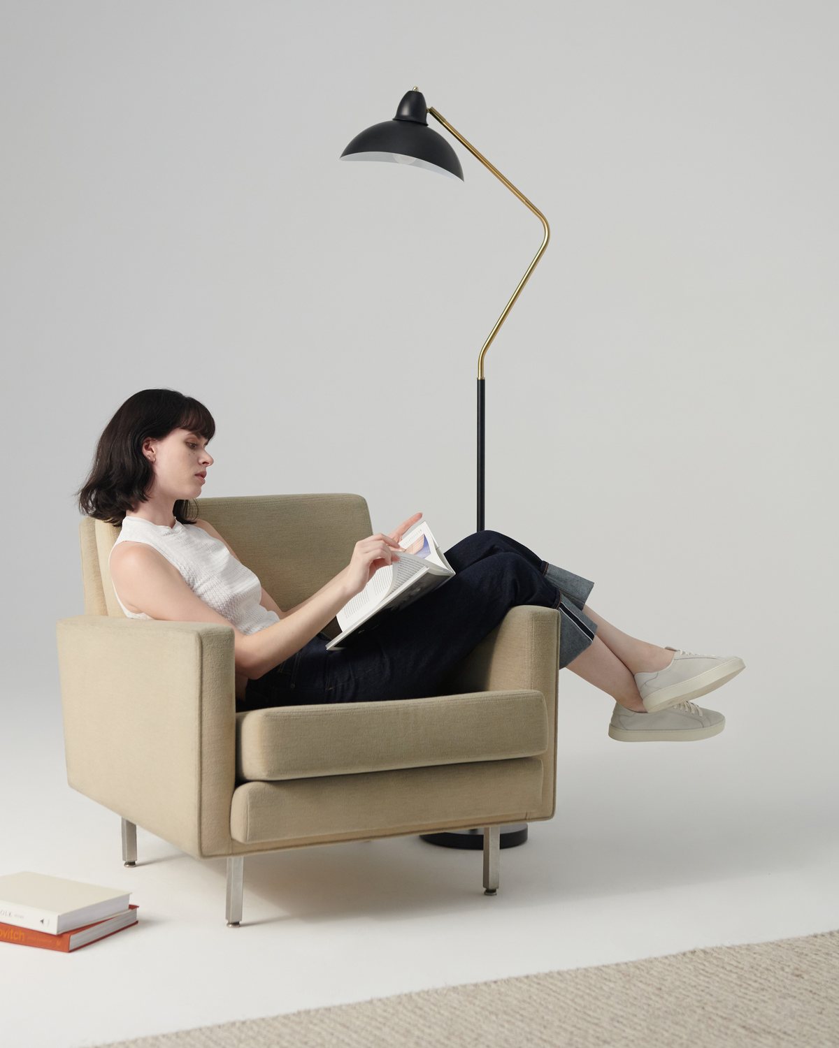 Black Brightech Swoop floor lamp with a brass arm angled over a woman reading in an armchair