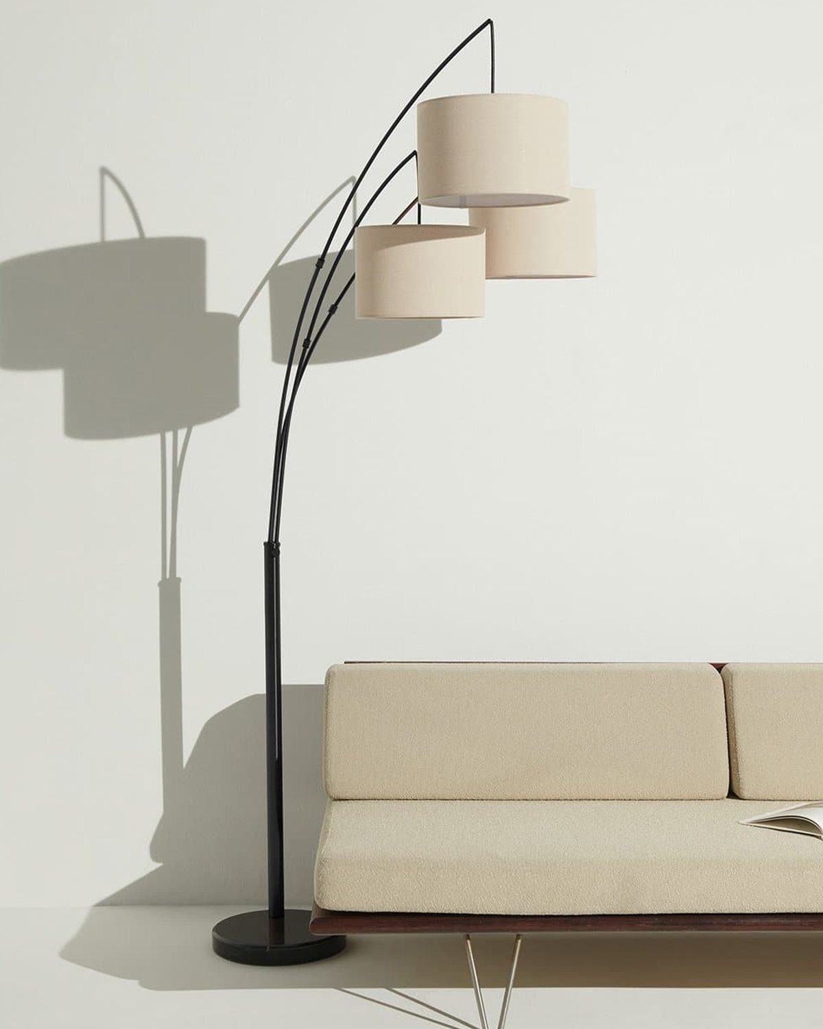 Black Brightech Trilage floor lamp with three linen shades arching over a cream sofa