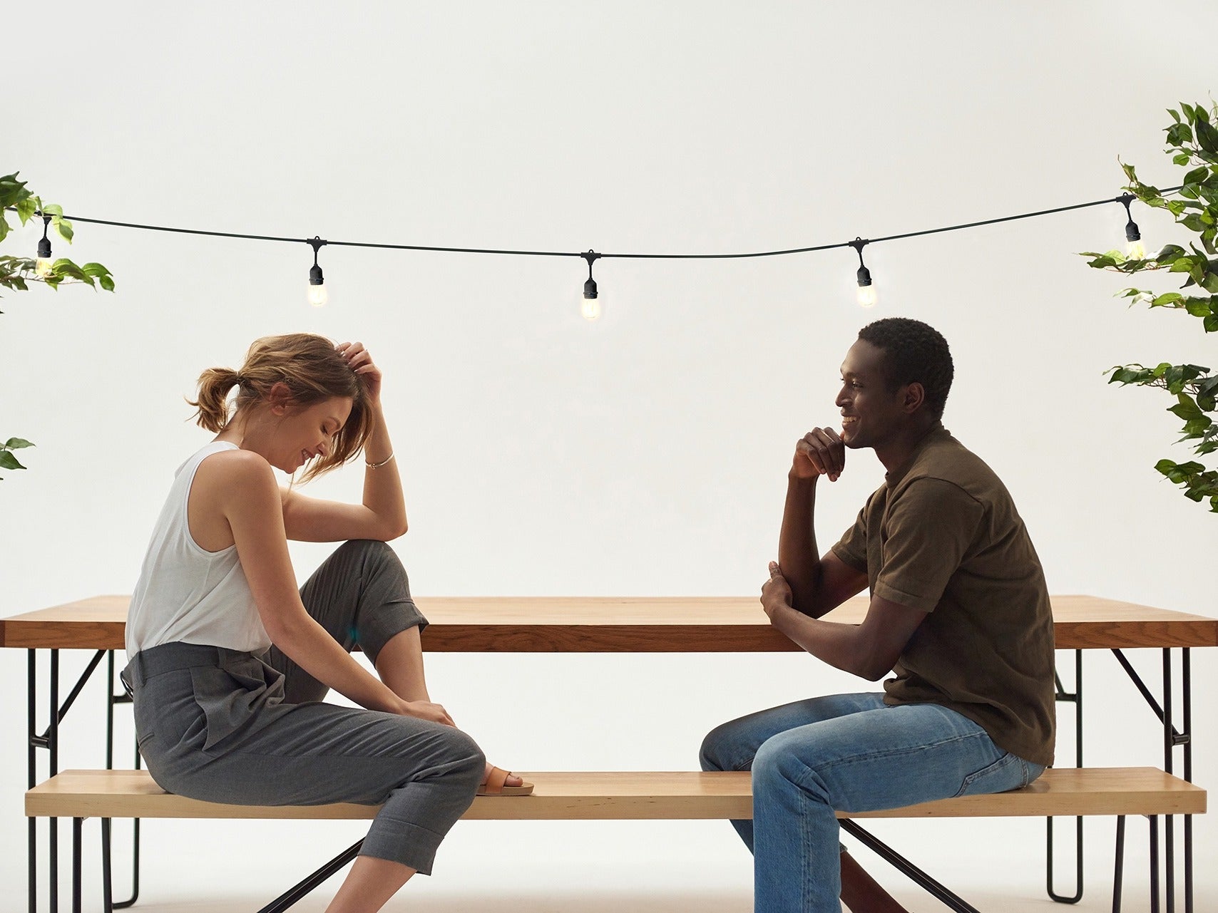 Two people talking at a wooden picnic table under Brightech Ambience Pro string lights