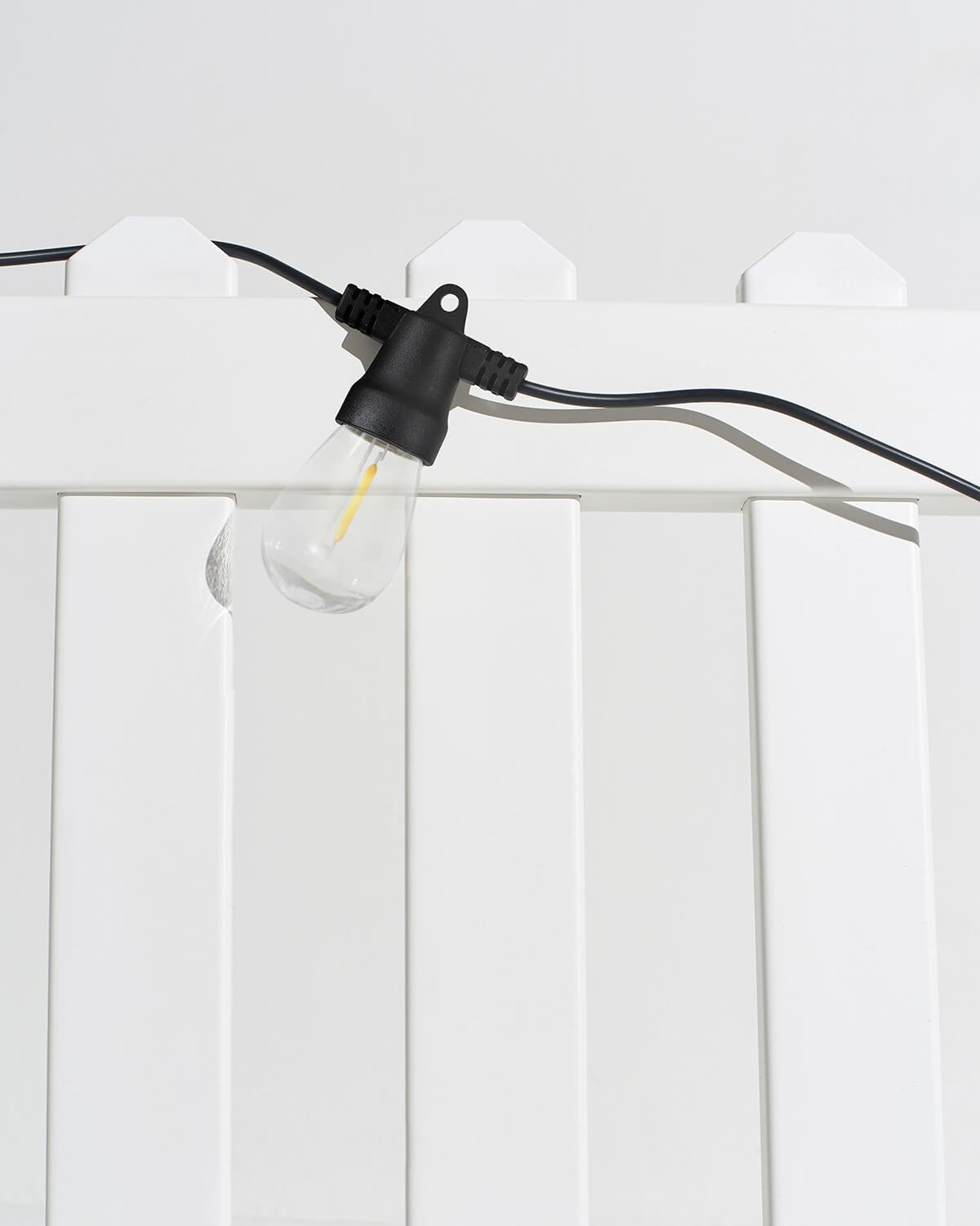 Brightech Ambience Pro Solar string light bulb hanging over a white fence