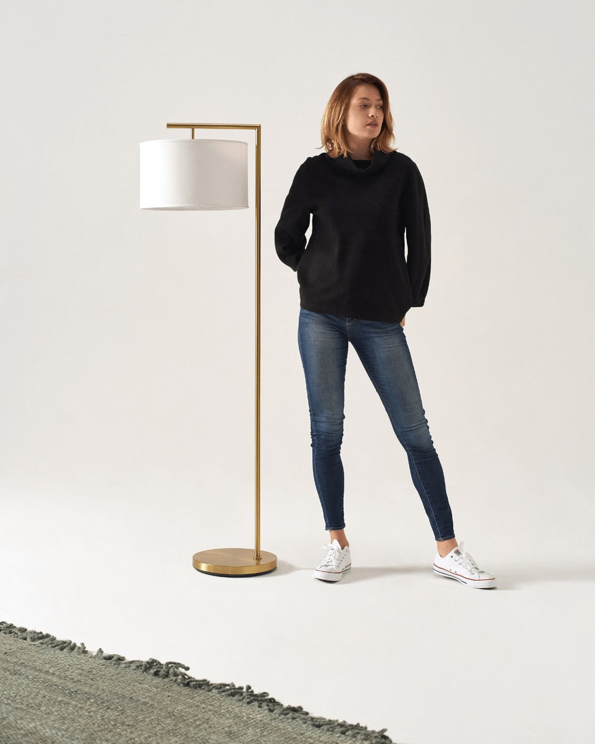 Woman standing beside an antique brass Brightech Montage Modern floor lamp with a white drum shade