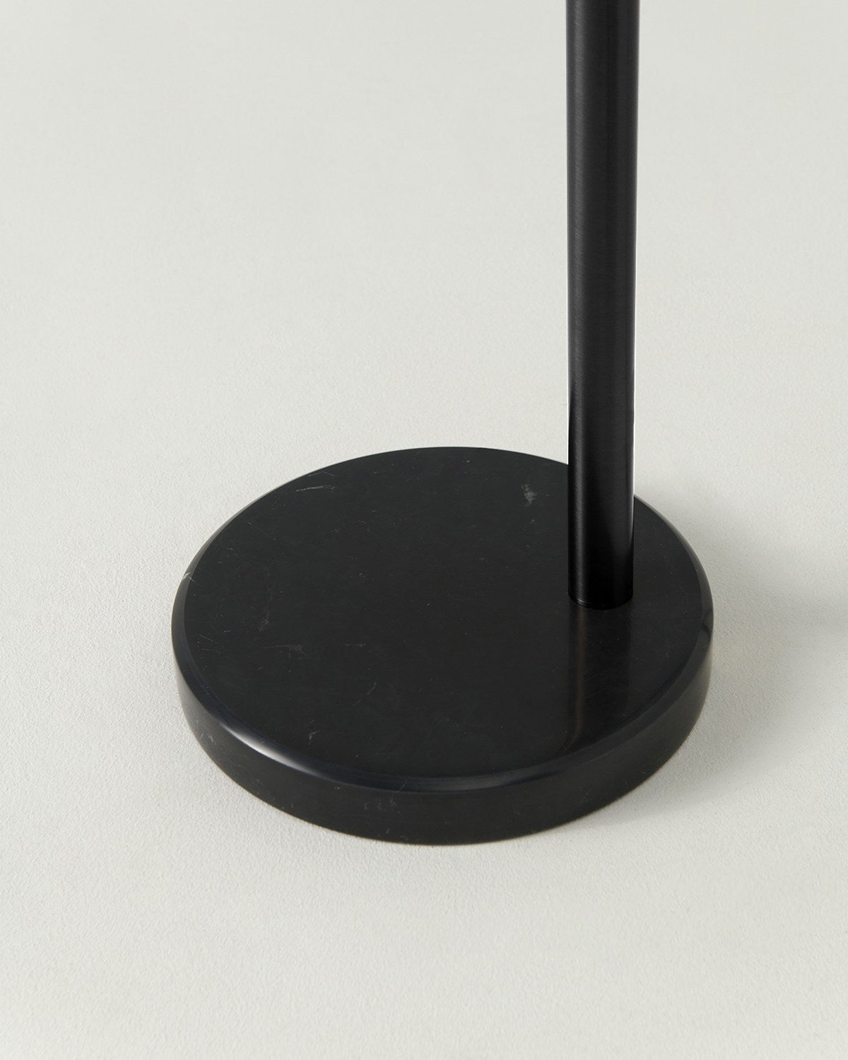 Close-up of the round black marble base and black pole of the Brightech Trilage floor lamp