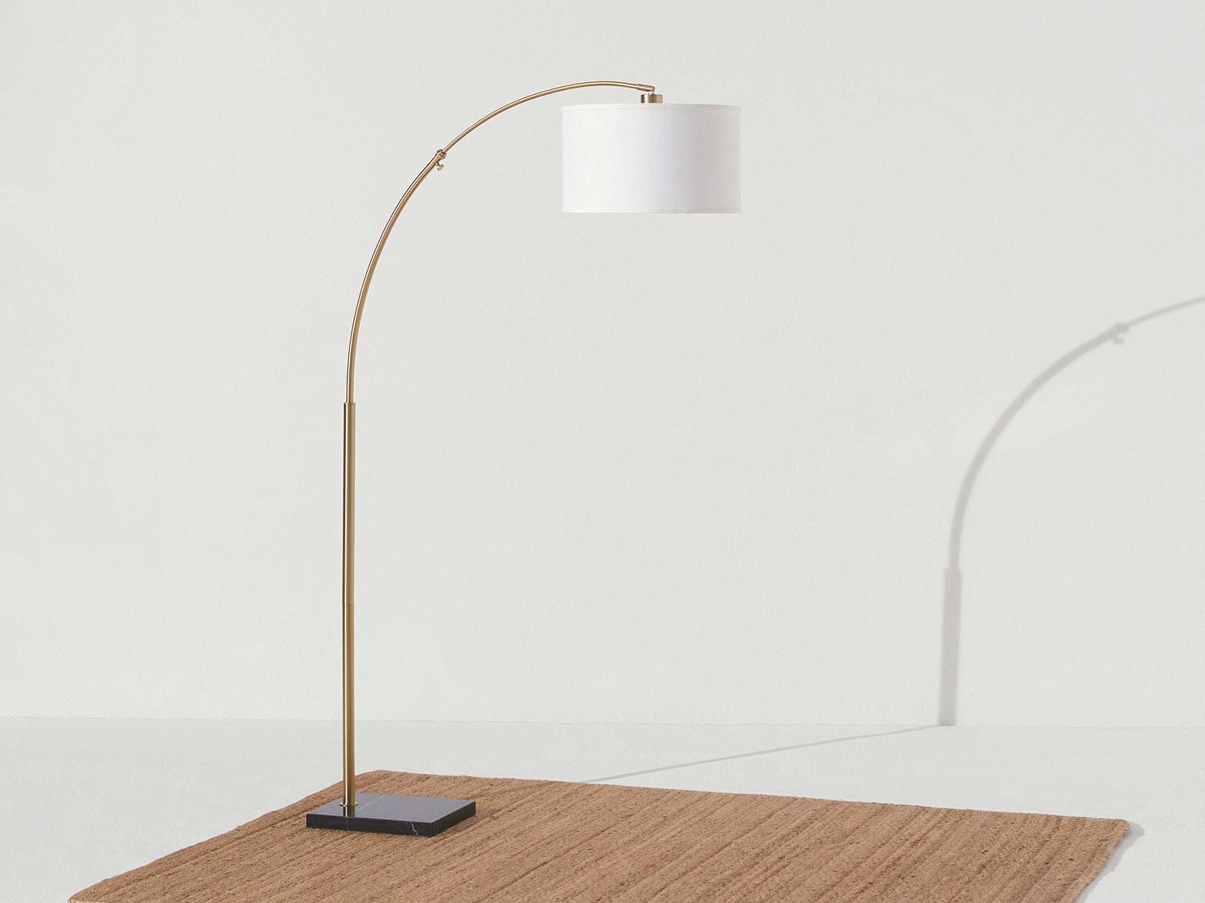 Brass Brightech Logan arc floor lamp with a white drum shade arching over a jute rug