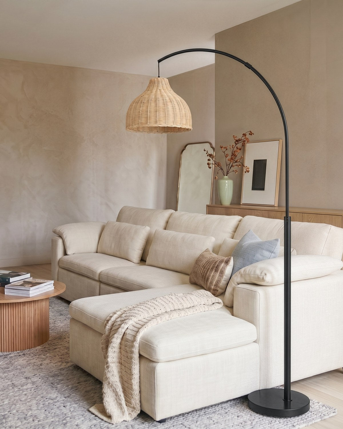 Black Brightech Lark arc floor lamp with a woven rattan shade arching over a cream sectional sofa