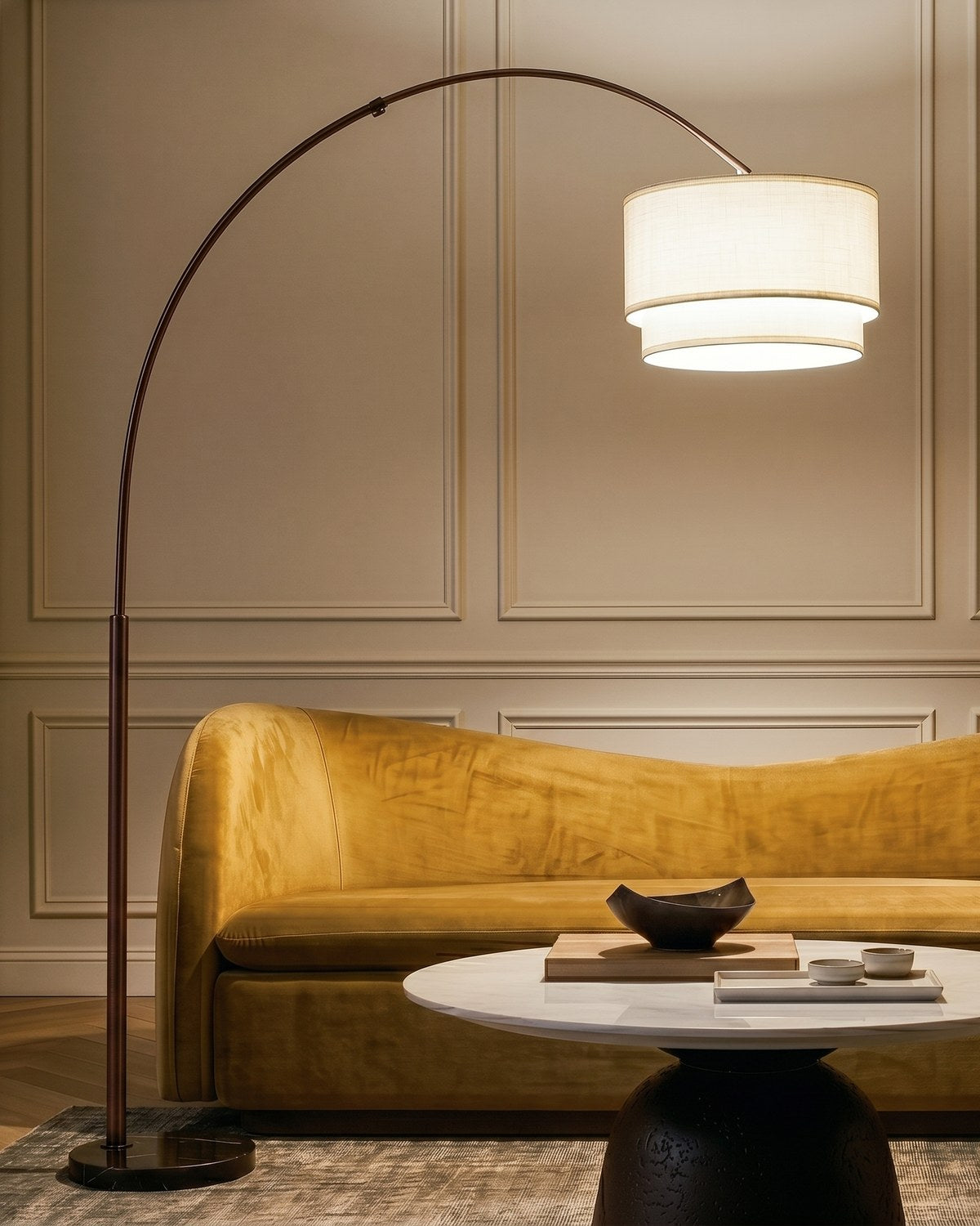 Dark bronze Brightech Mason arc floor lamp with a lit double drum shade arching over a mustard velvet sofa