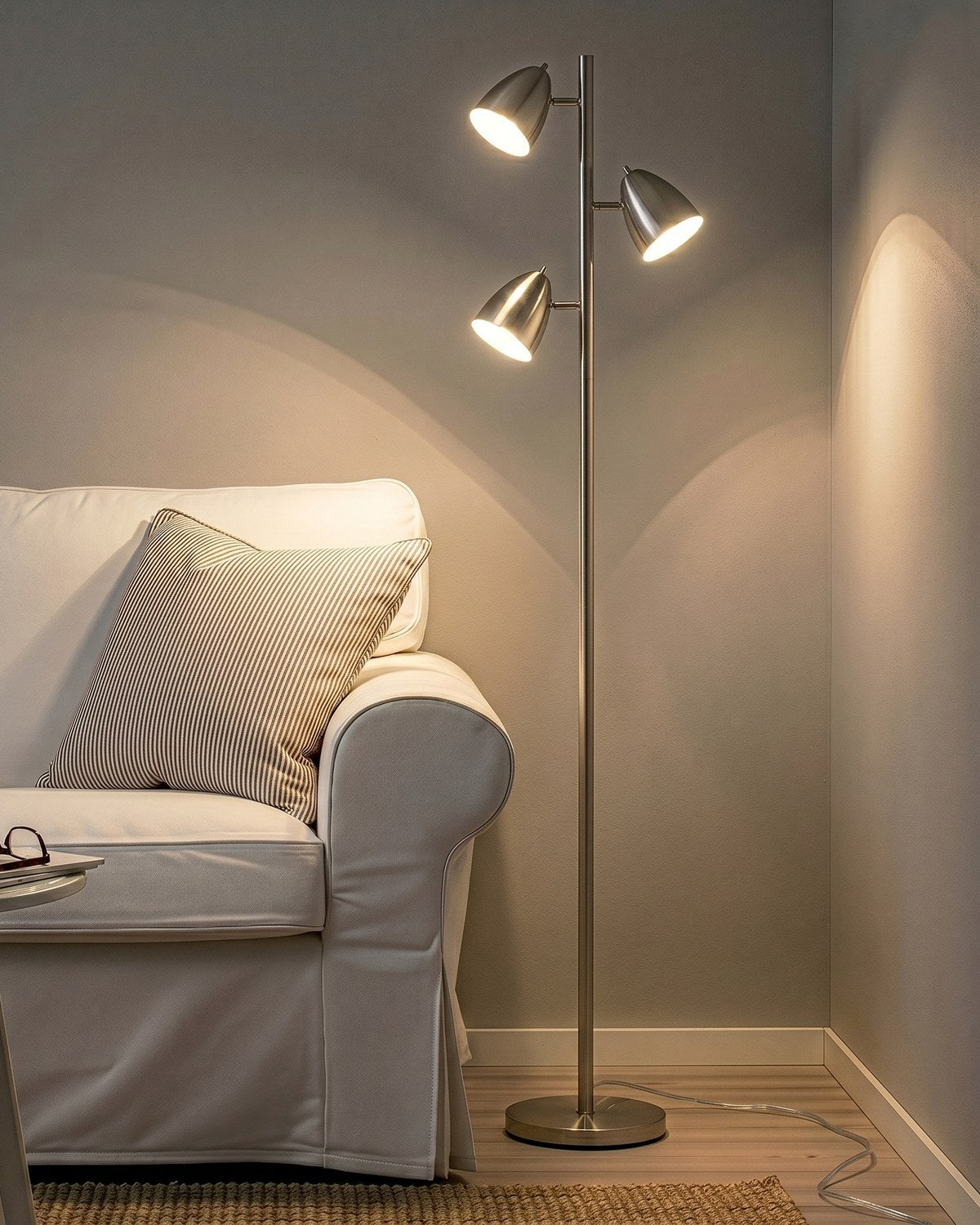 Nickel Brightech Jacob floor lamp with three lit swiveling shades beside a white sofa