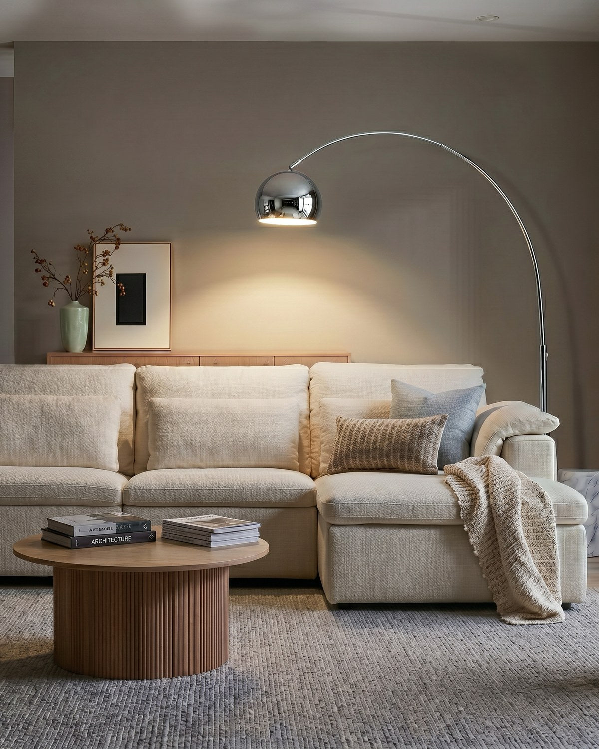 Chrome Brightech Olivia arc floor lamp reaching its globe shade over a cream sectional sofa
