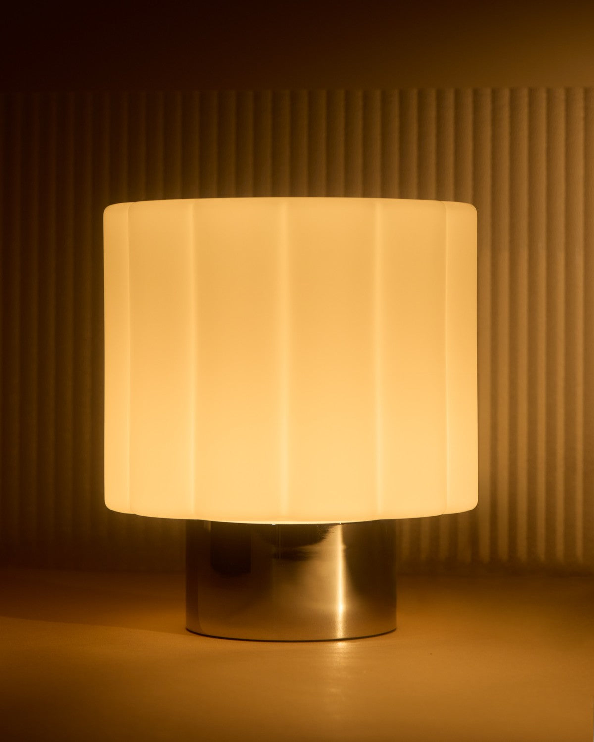 Lit Brightech Addison table lamp glowing warm amber above its chrome base