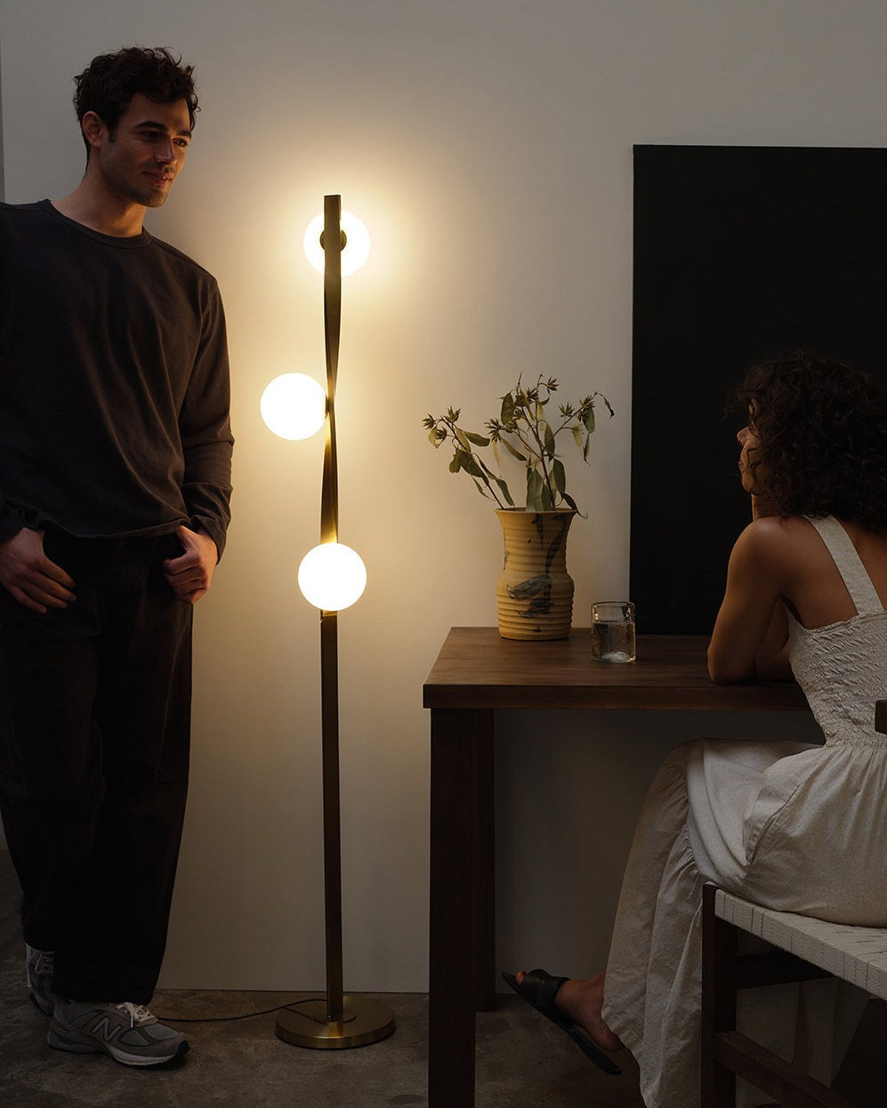 Brightech Nola floor lamp with three glass globes glowing in a dim room with two people